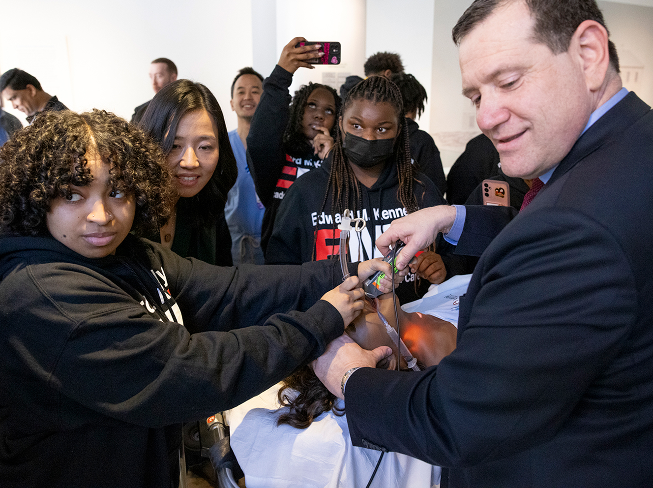 Students from the Edward M. Kennedy Academy of Health Careers and Boston Mayor Michelle Wu work together to “take care” of a simulated patient with Mass General Chief Learning Officer James Gordon, MD.