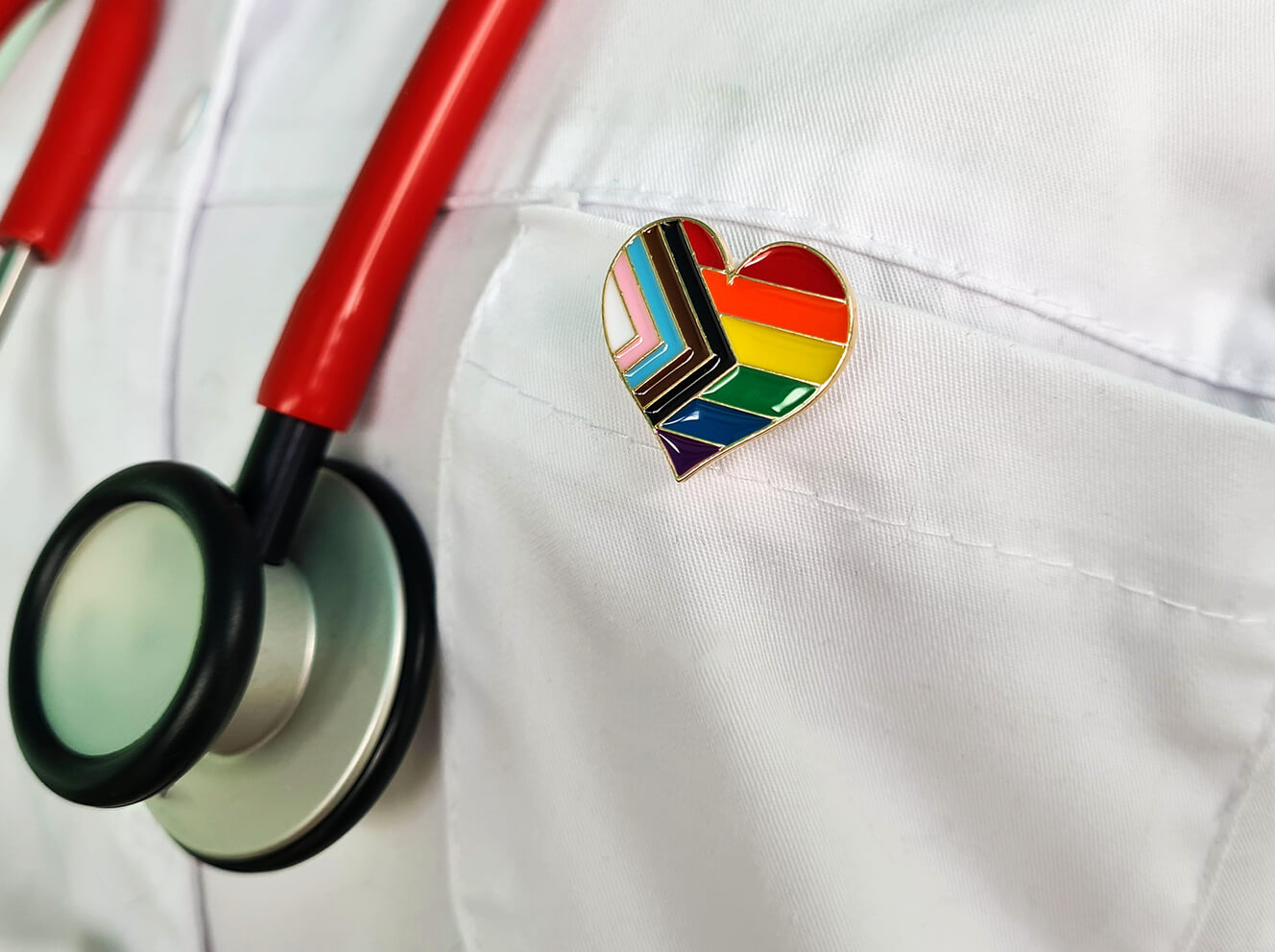 doc with stethoscope and LGBTQIA+ pin on white coat